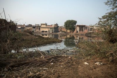 The picture shows a stagnant pool of polluted water near buildings in Pakistan